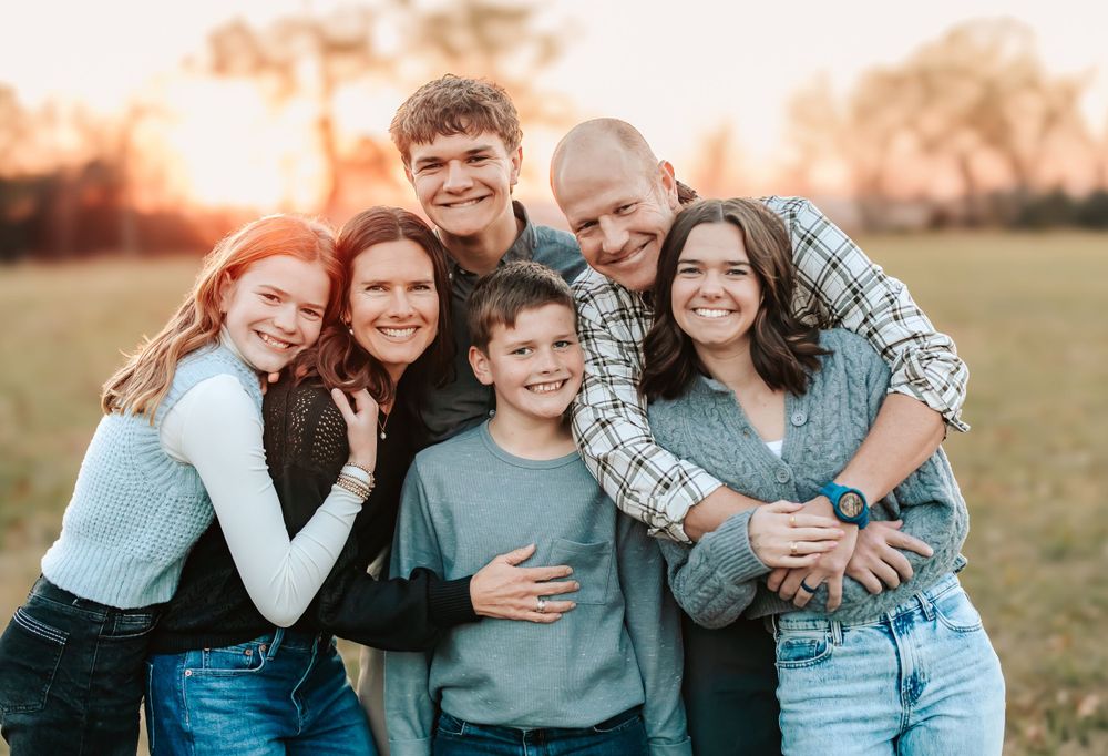 A close-knit family group poses together outdoors at sunset in a grassy field.