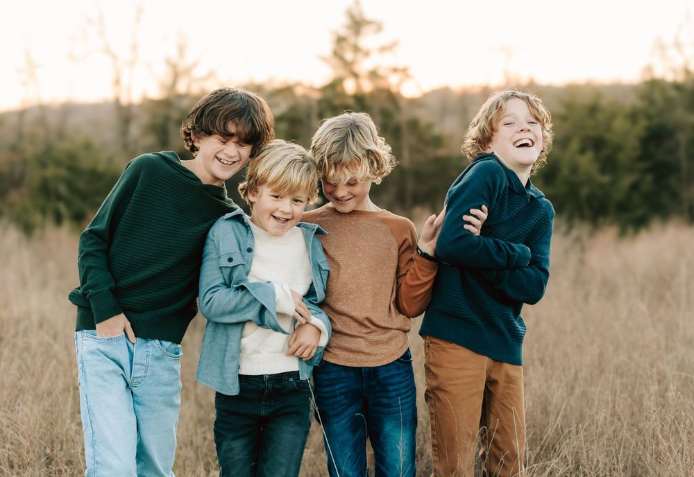 A group of siblings in sweaters share a joyful candid moment together in a sunlit autumn field.