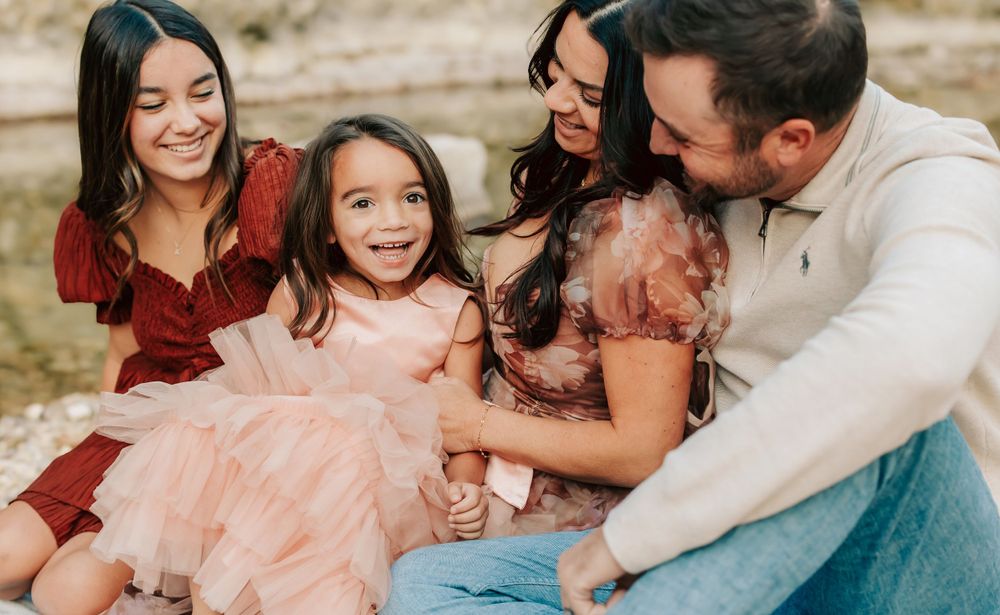 Family sitting together outdoors sharing a joyful moment in casual attire with burgundy and pink clothing.
