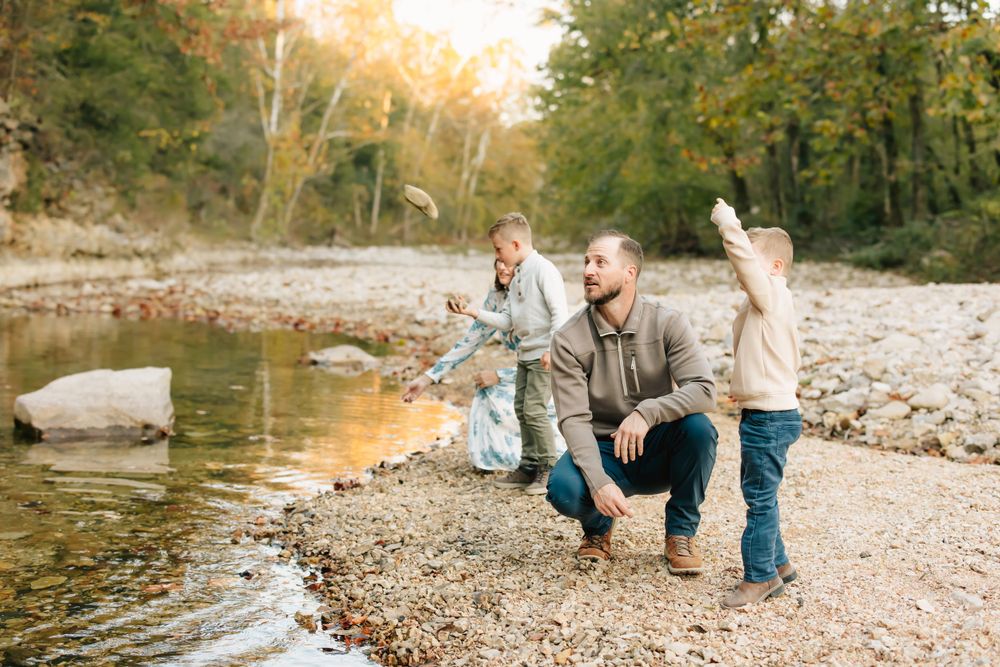 Three people enjoying a golden hour by a riverside with rocks and trees in the background during autumn.