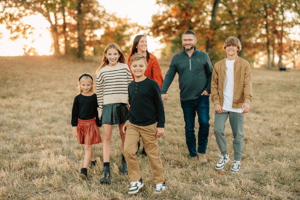 A family of five walking together in a golden autumn field at sunset wearing casual fall clothing.