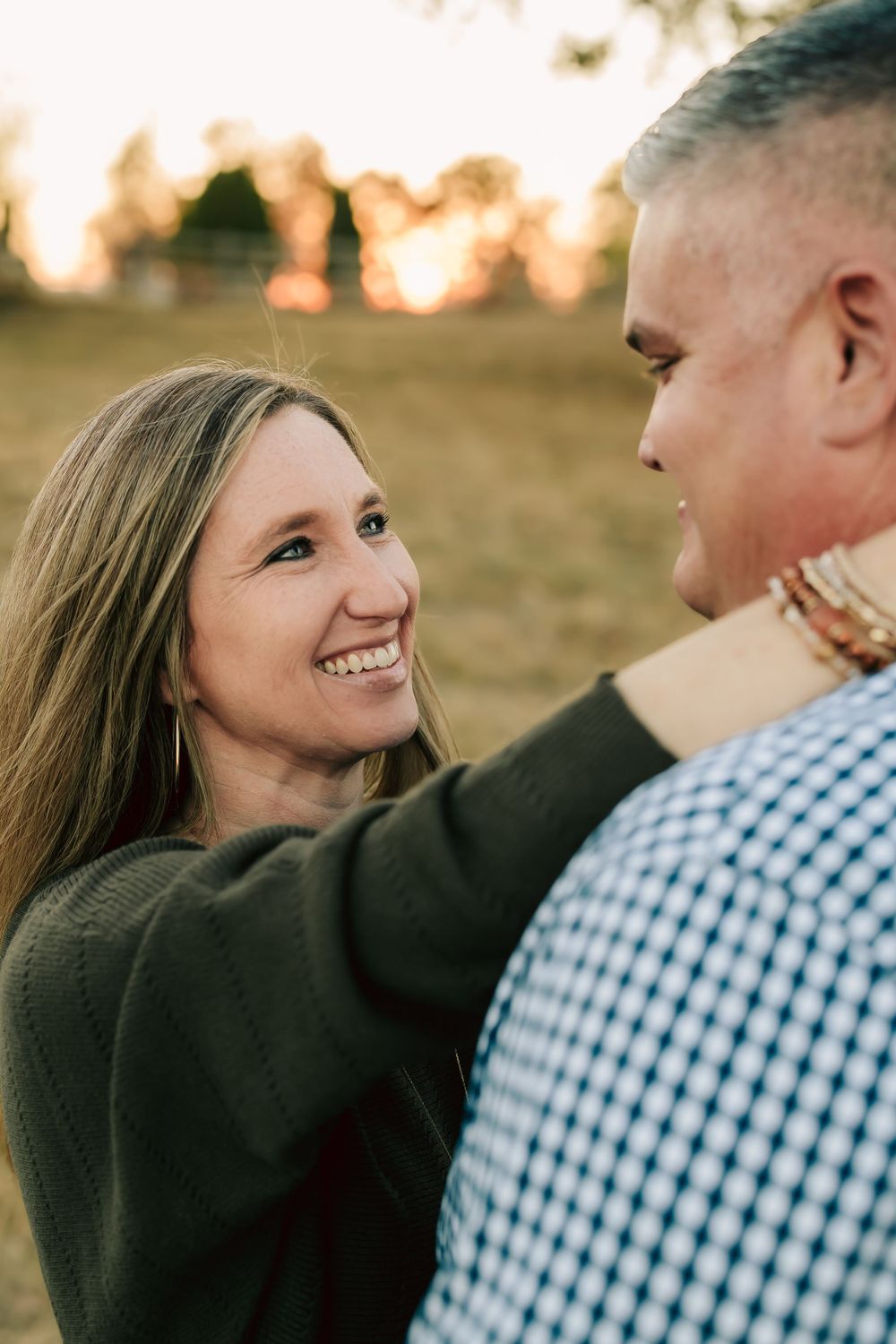 A couple shares an intimate moment at sunset outdoors with one wearing a plaid shirt and the other a dark sweater.
