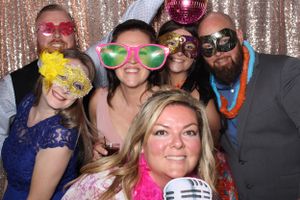 Large group of adults enjoying Flawless Photos Photo Booth with fun props at a wedding.