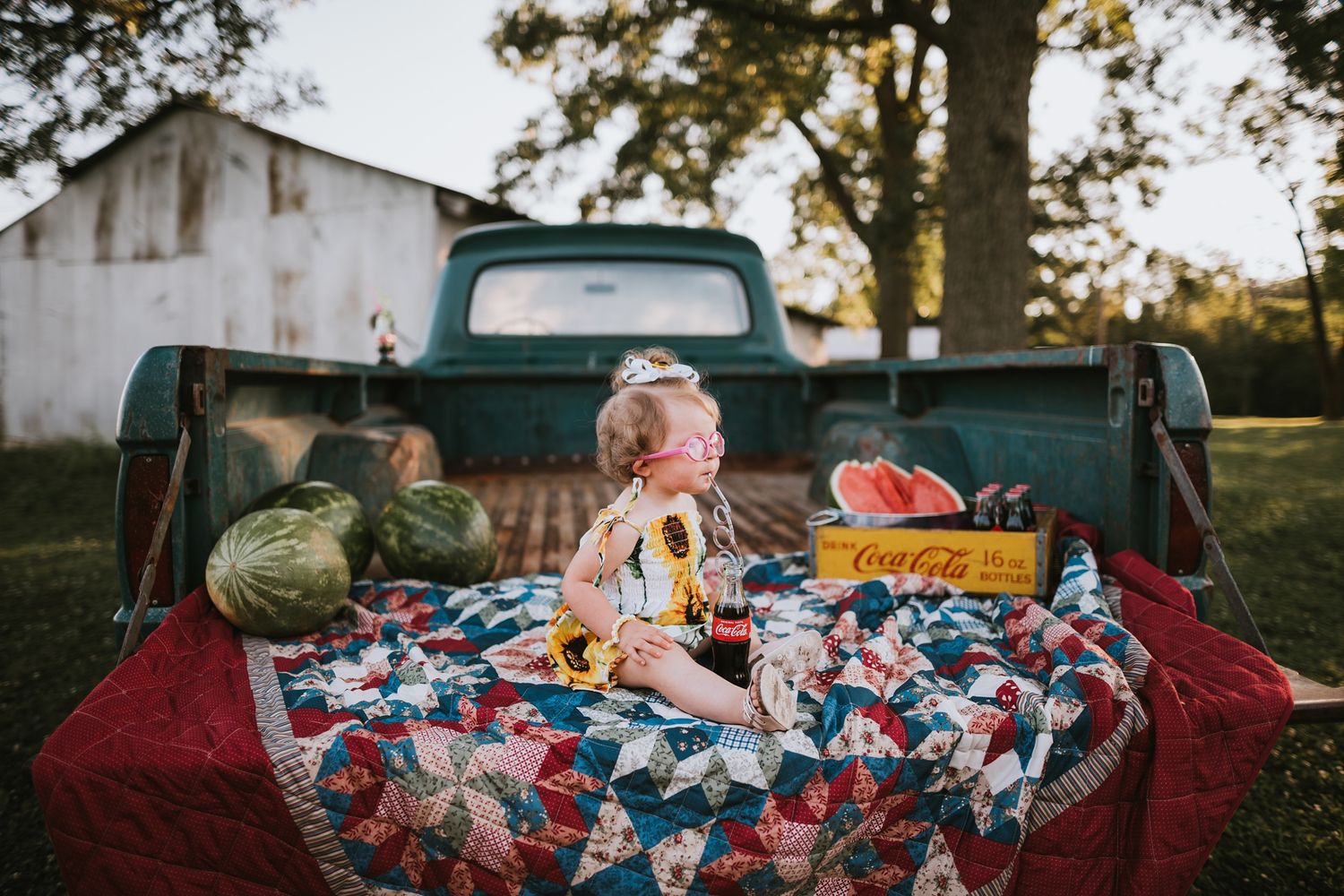 A vintage truck bed with fall harvest items including pumpkins and produce displayed on a red blanket.