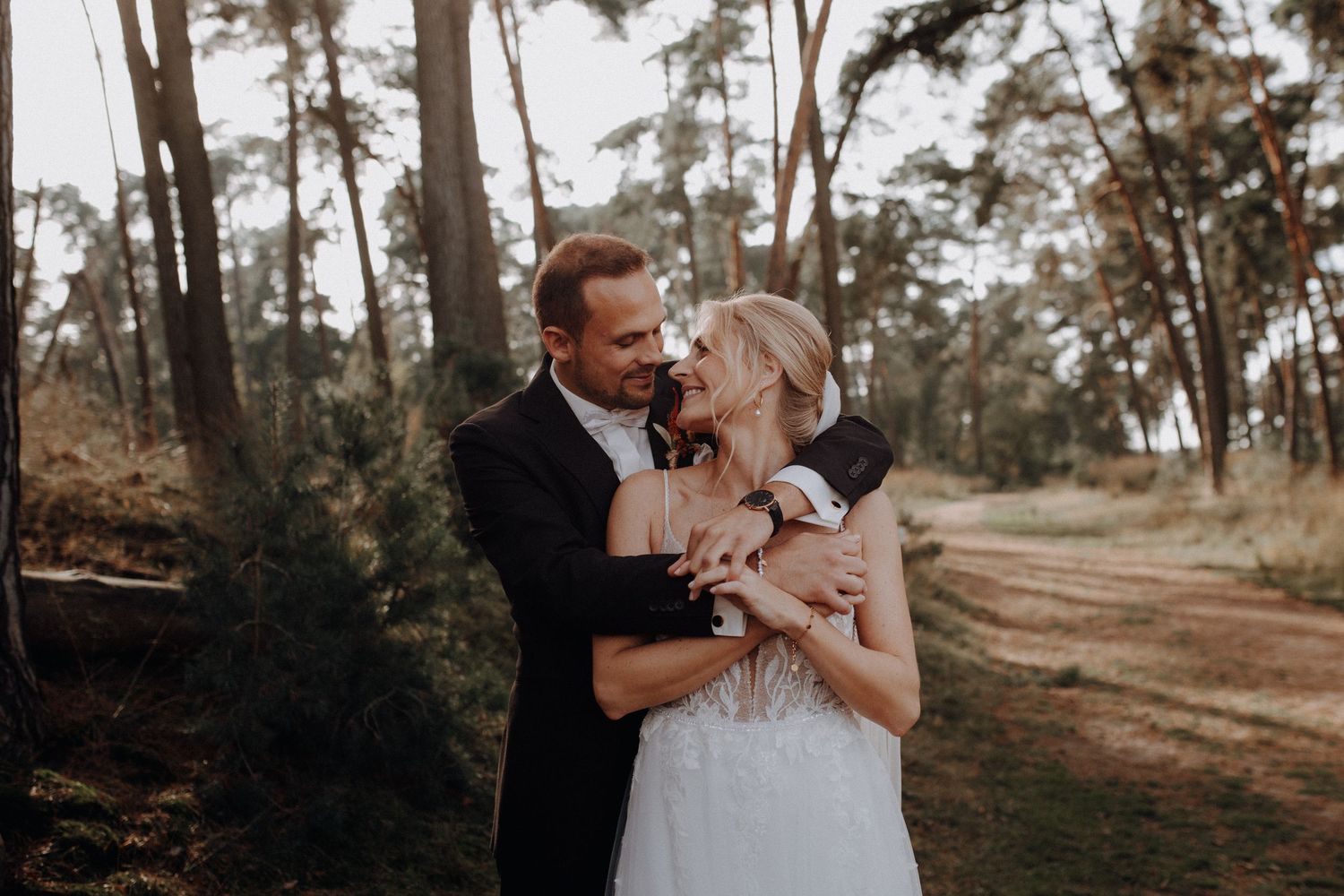 Bride and groom embracing tenderly in a sunlit forest path on their romantic wedding day.