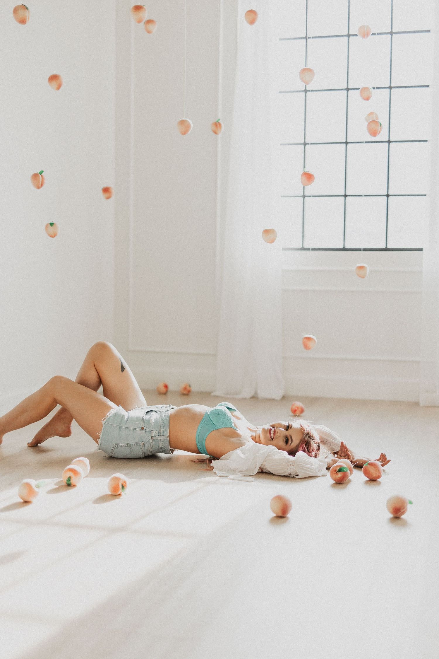 Person lying on white floor surrounded by scattered oranges in bright minimalist room interior.