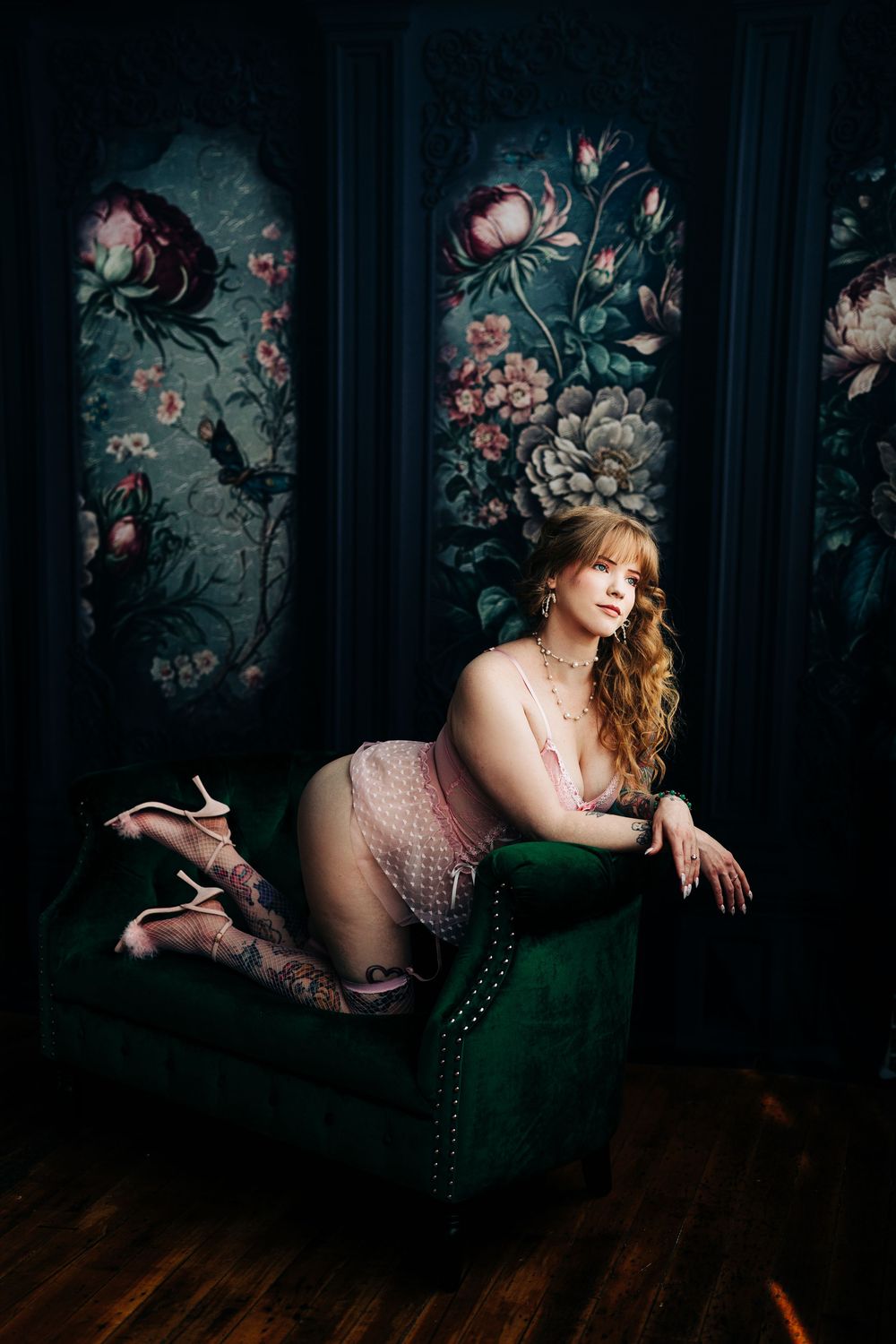 Romantic boudoir photographer in Loganville with portrait against dark floral wallpaper with figure reclining on emerald green velvet chaise