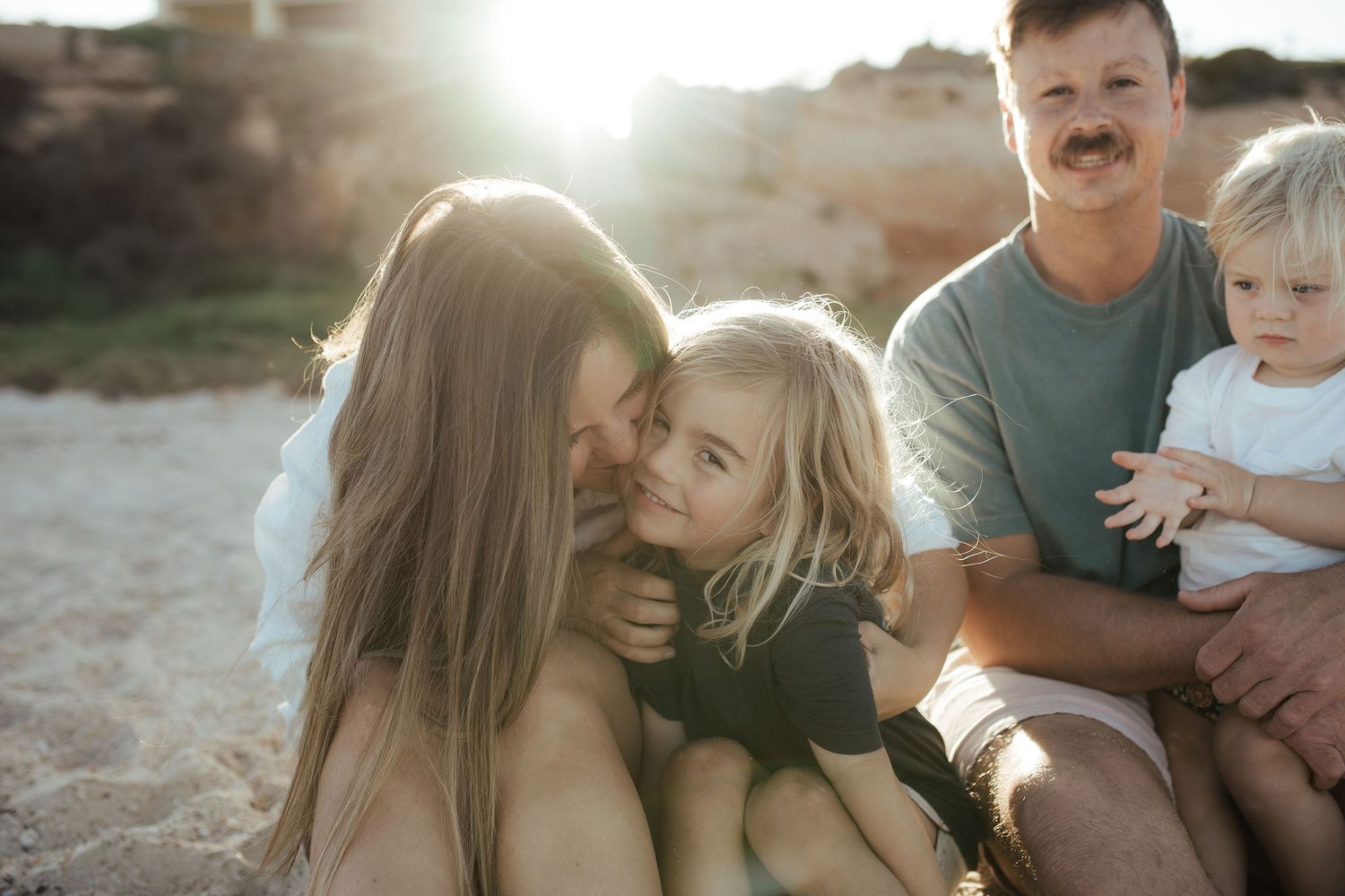 Family sharing intimate moment on beach during golden hour sunset.
