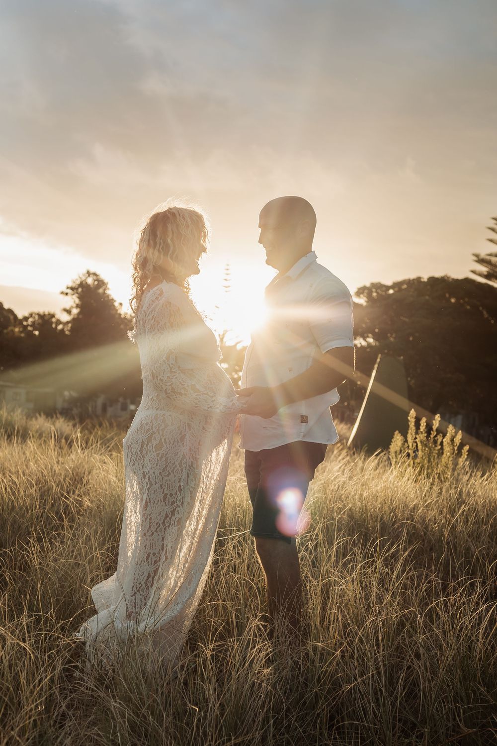 Couple holding hands in golden grass field with stunning sunset lens flare.