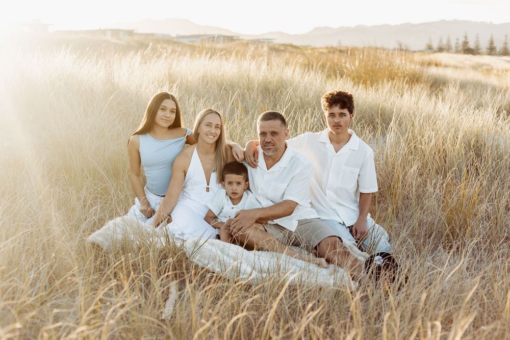 Happy family of five sitting together in golden grass field at sunset.