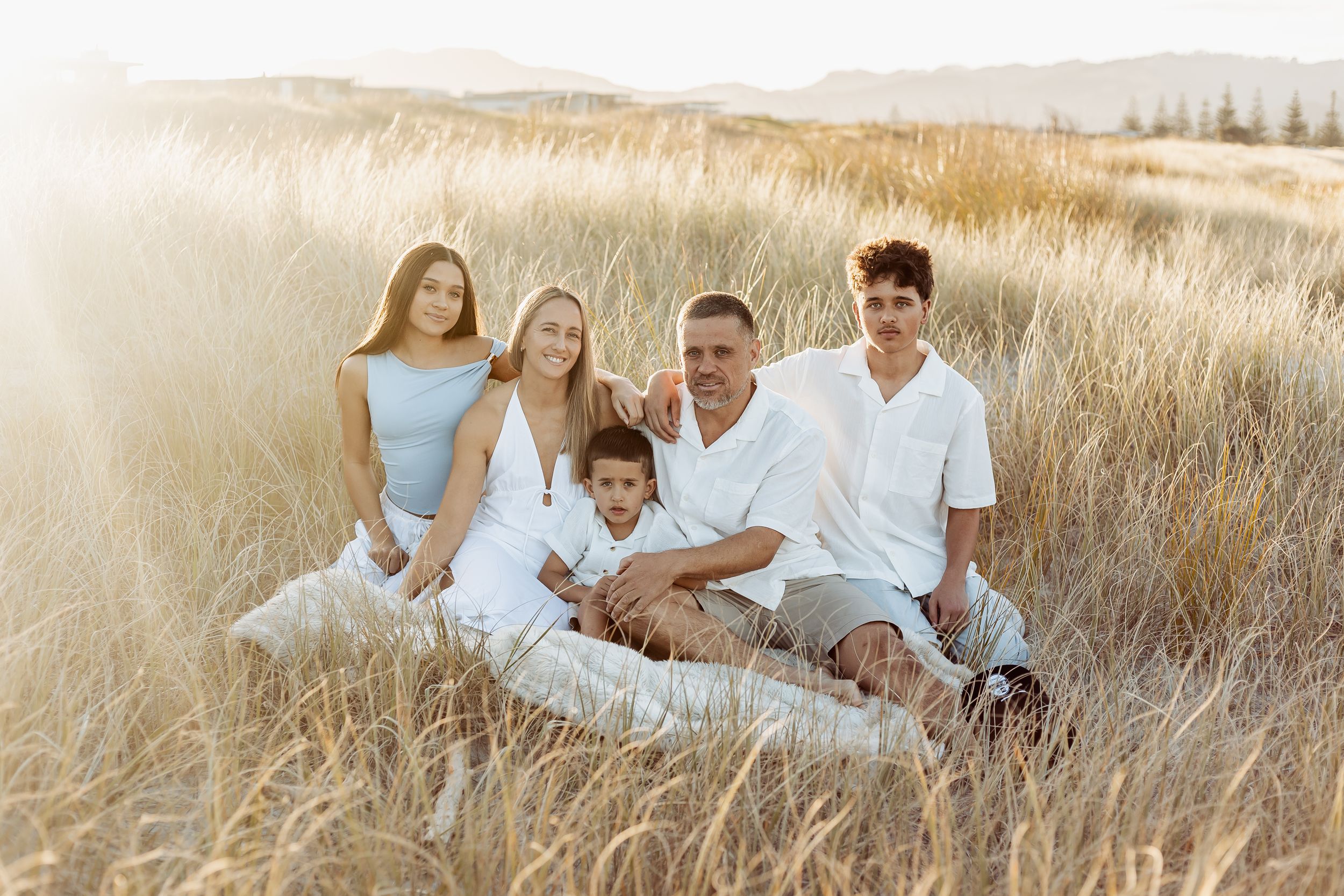 Happy family of five sitting together in golden grass field at sunset.