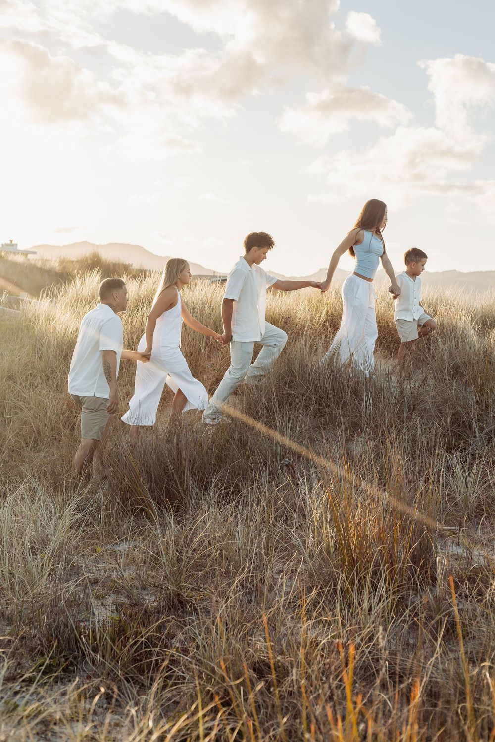 Family holding hands walking through tall golden grass dunes at sunset.