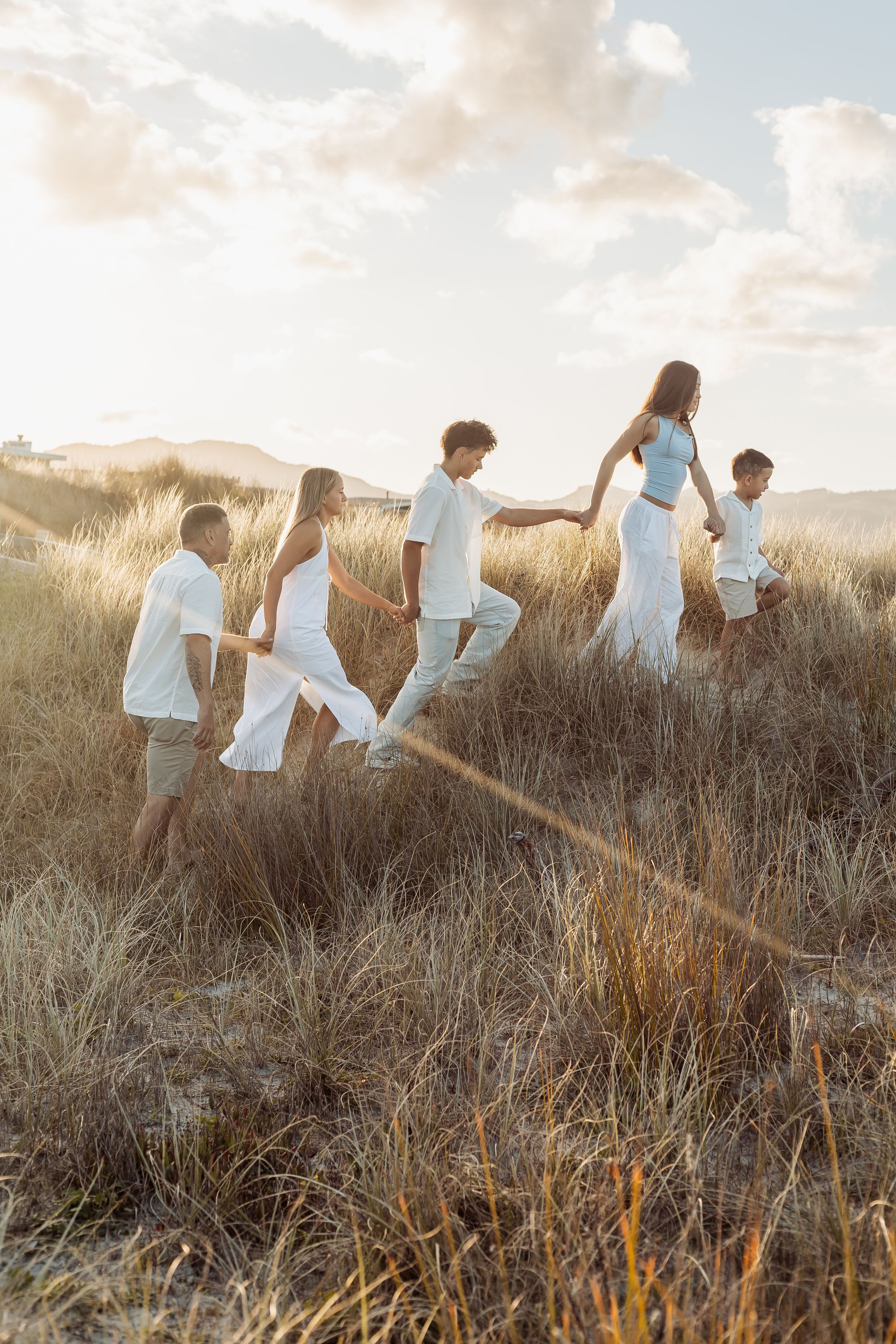 Family holding hands walking through tall golden grass dunes at sunset.