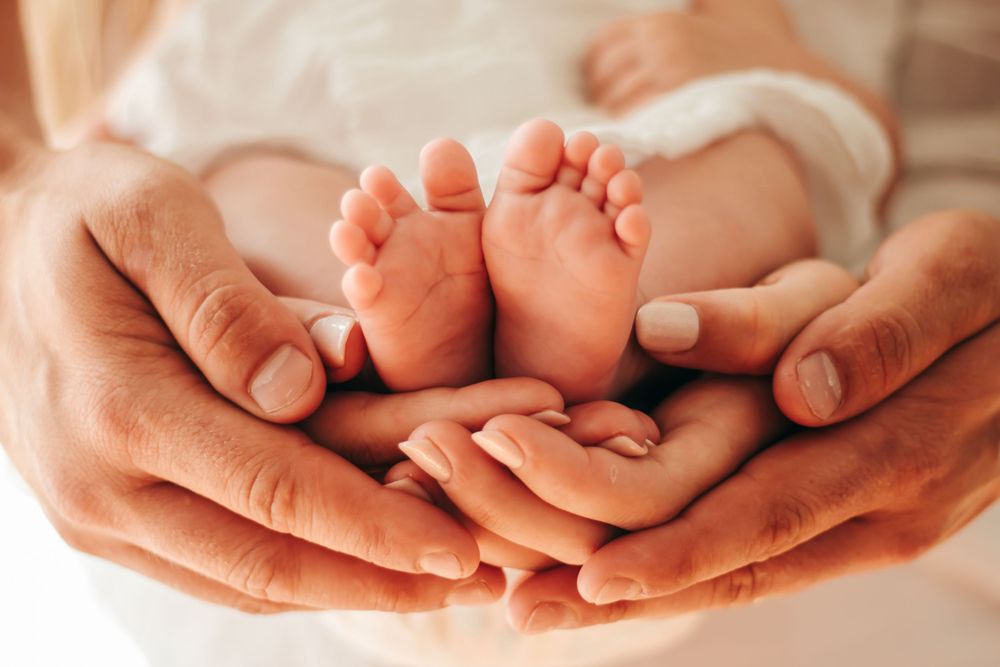 Parents cradling newborn baby feet in their hands, close-up of tiny infant feet.