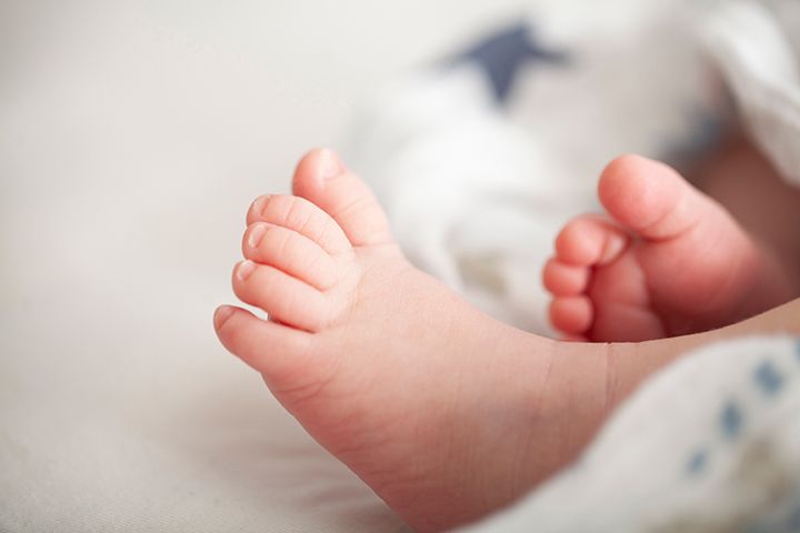 Close-up view of tiny newborn baby feet with pink toes against a soft white background.