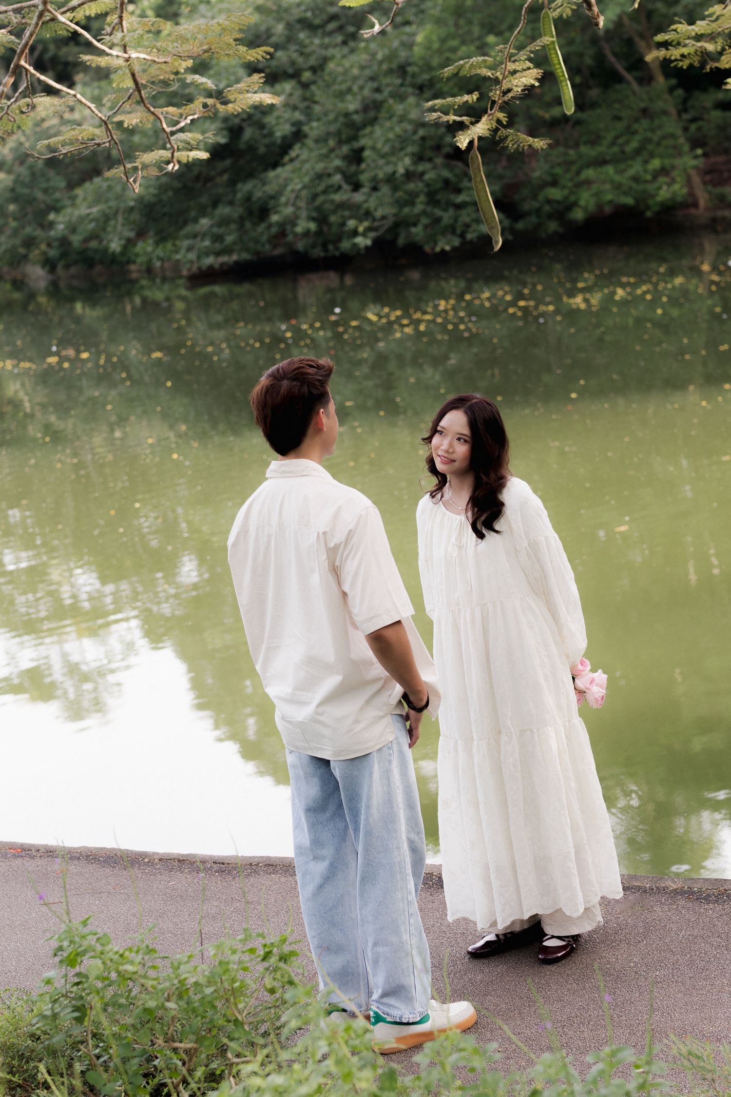 Couple walking together on a grassy hill with white buildings in the background.