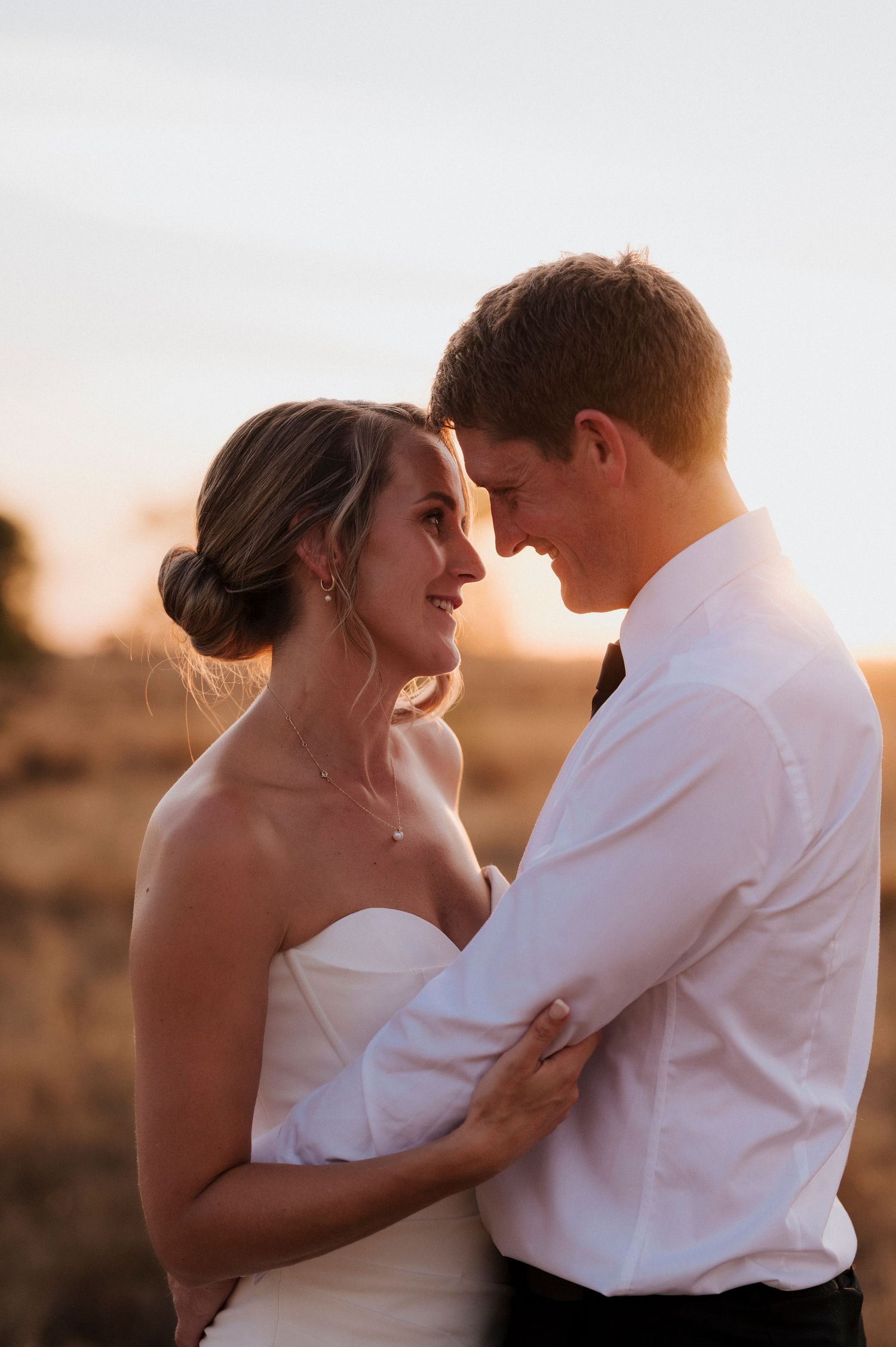 Romantic sunset portrait of newlyweds sharing an intimate moment in formal wedding attire.
