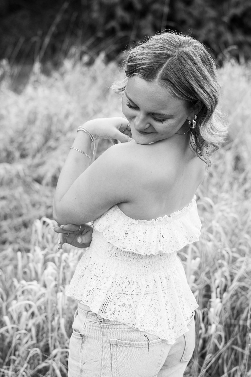 Black and white portrait of a person in a white lace top posing in a field of tall grass.