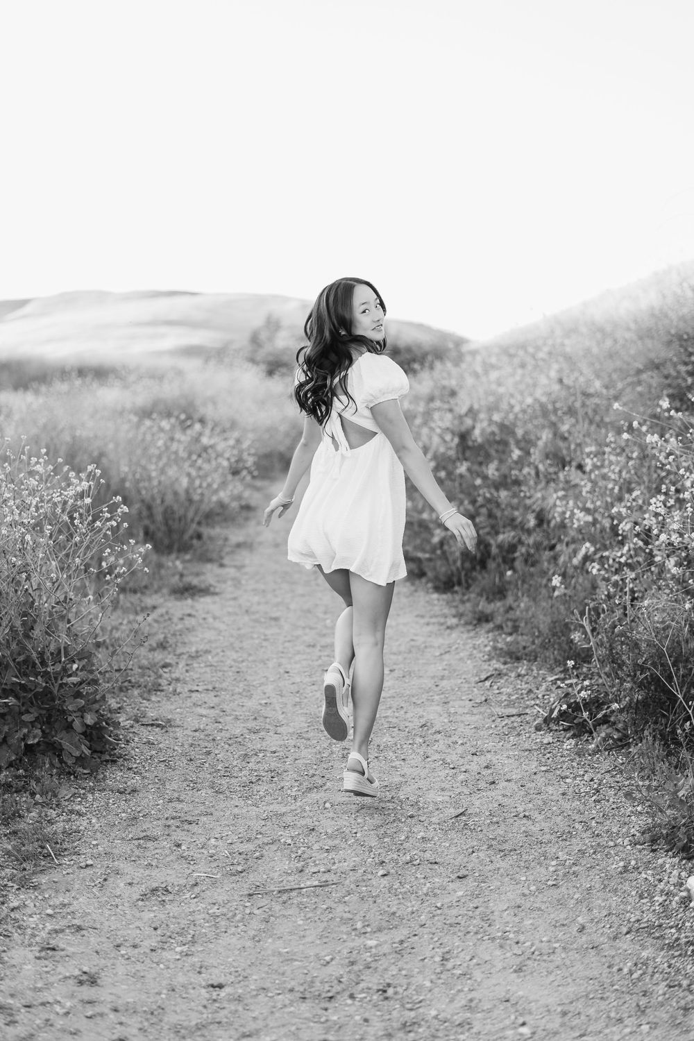 Black and white photo of someone running joyfully down a nature path surrounded by wildflowers.