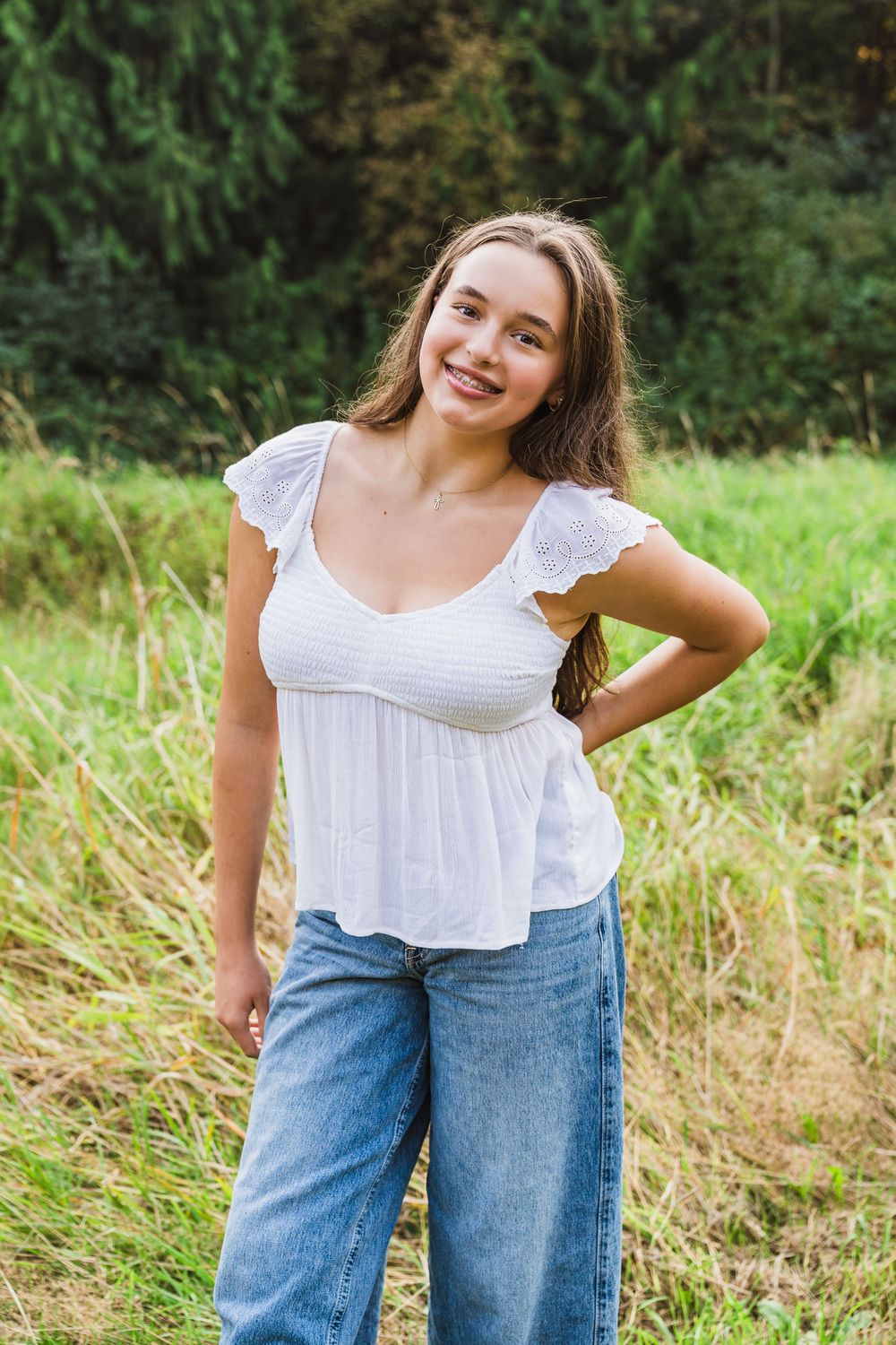 A person wearing a white ruffle blouse and blue jeans poses casually in a grassy outdoor field.
