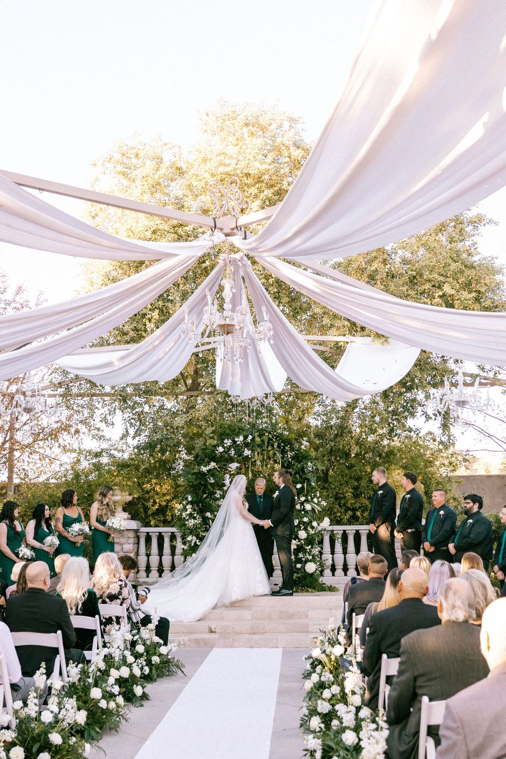 Elegant outdoor wedding ceremony with white draped fabric canopy and floral arrangements beneath a gazebo.