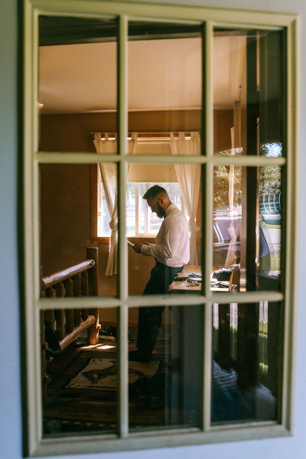 Looking through window panes at someone reading or studying at a desk in warm indoor lighting in Central Valley