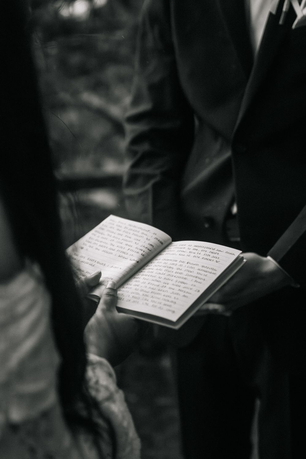 Black and white photo of hands holding an open journal or vow book during a wedding ceremony.
