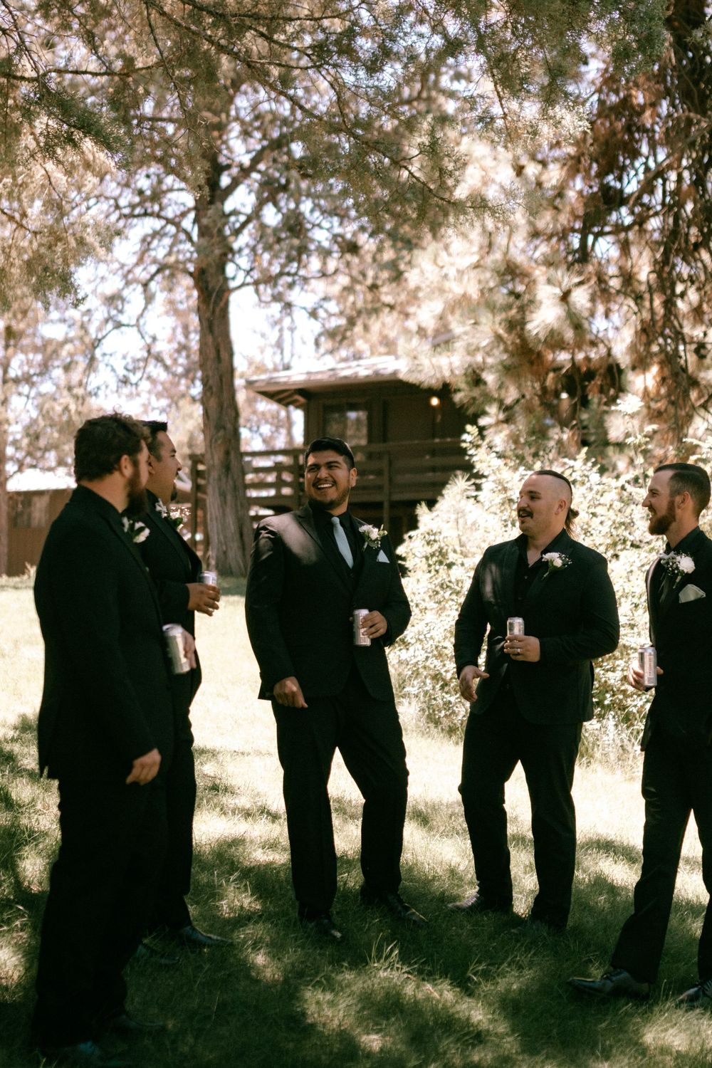 A group wearing dark formal attire standing together under sunlit trees during an outdoor event.