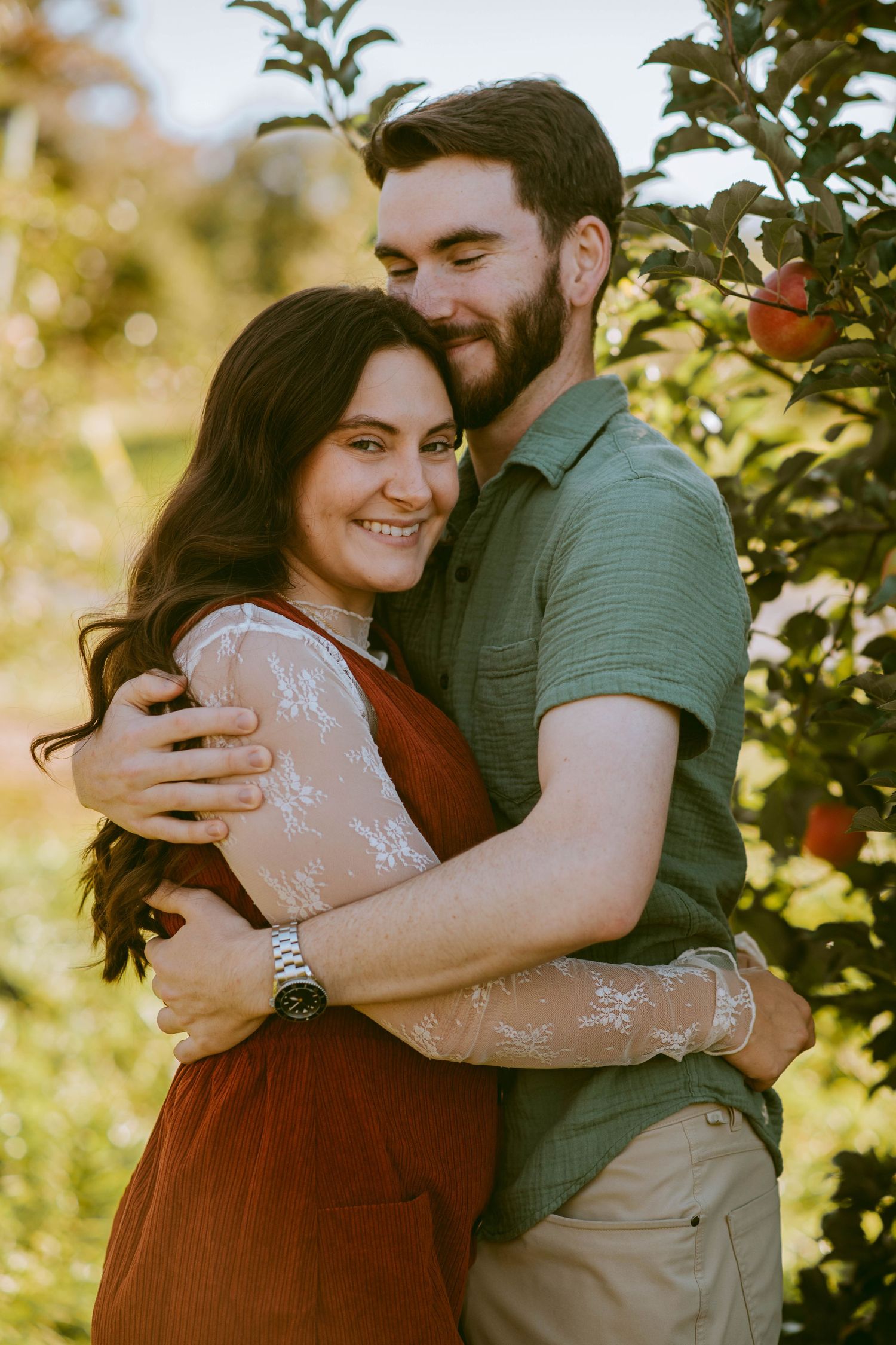 Man hugging his fiancee close in an apple orchard