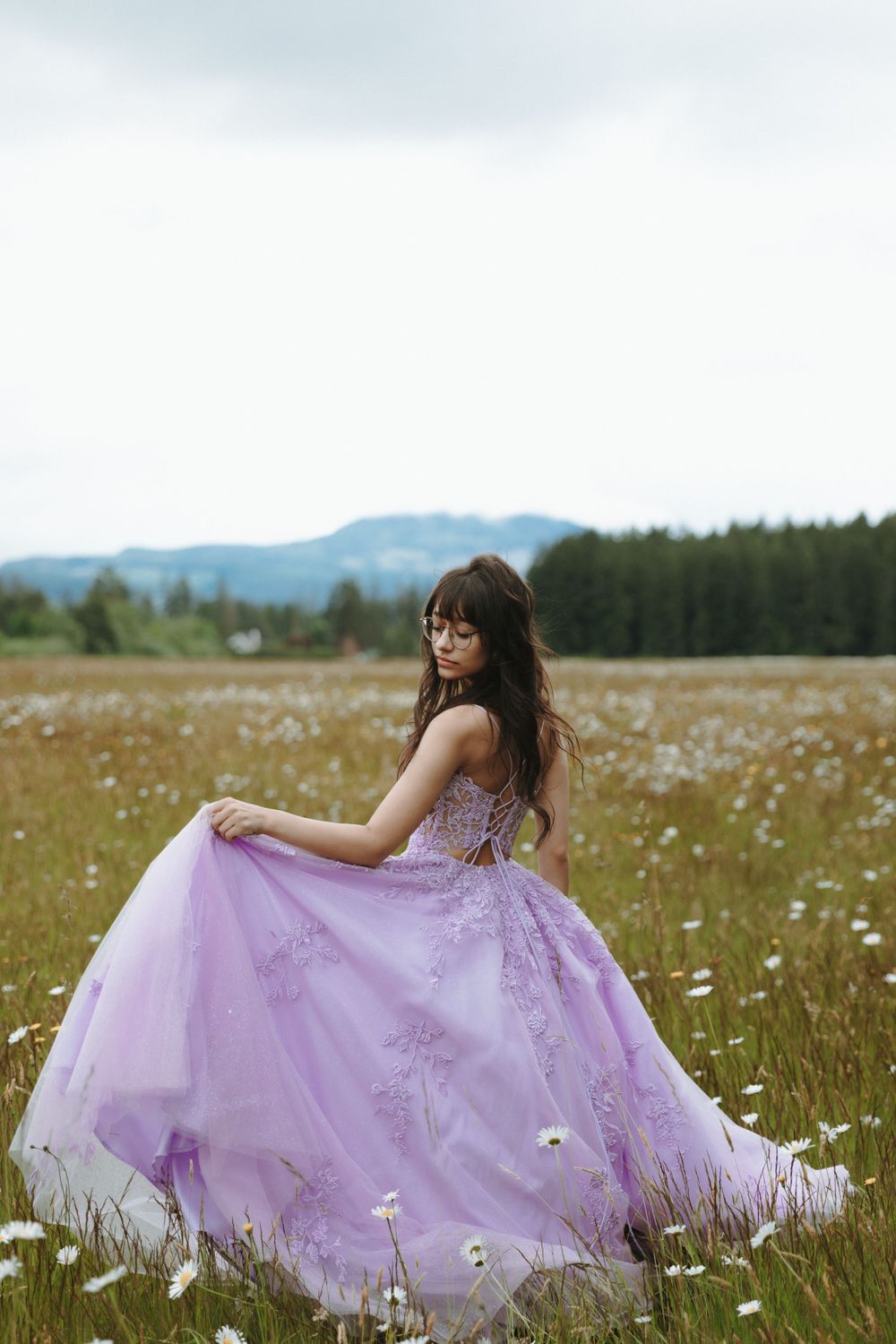 Purple ballgown dress flows gracefully in a wildflower meadow with mountains and forest in the background.