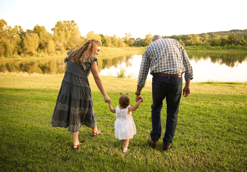 Family of three walking hand in hand toward a scenic lake at golden hour.