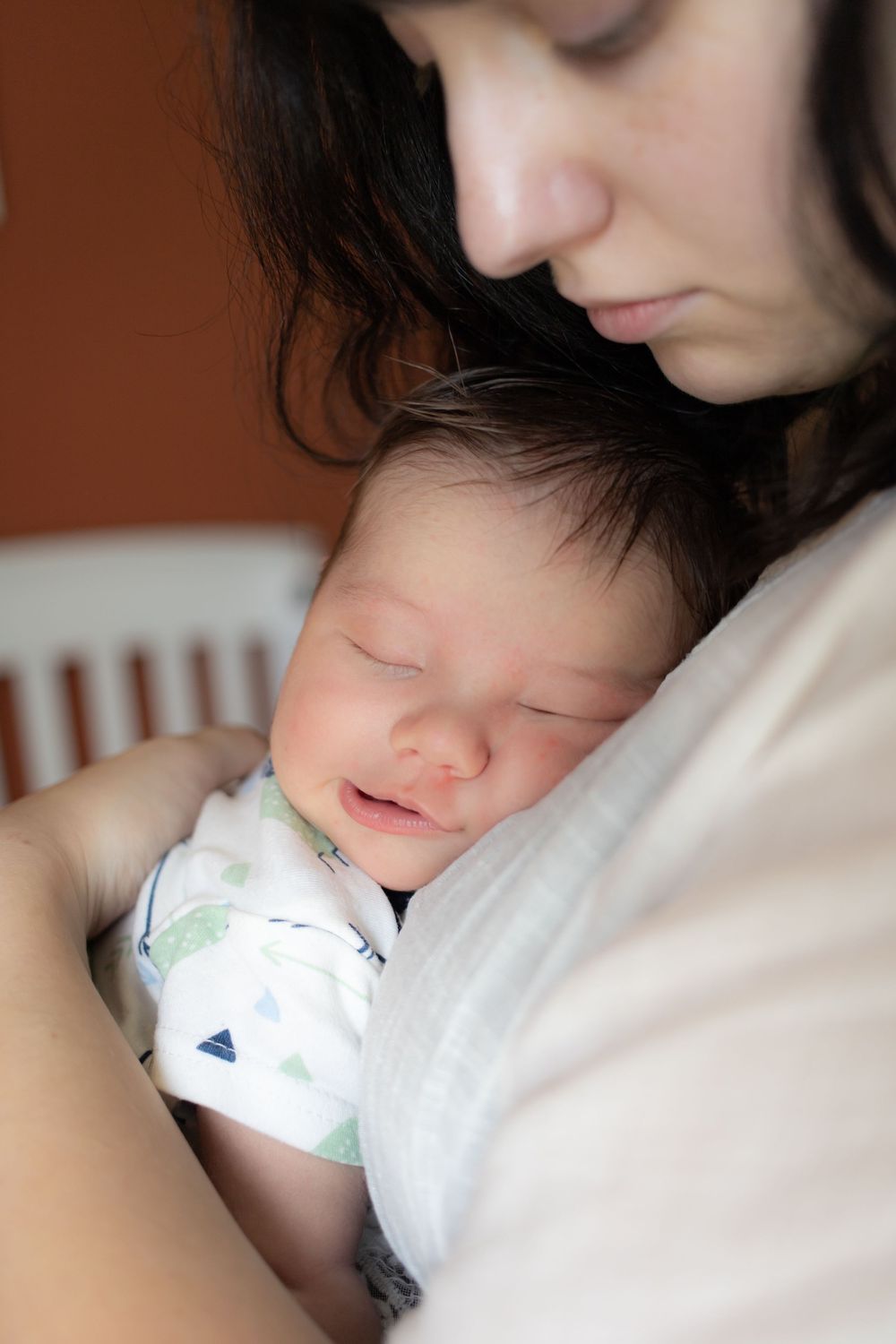 A mother tenderly holds her sleeping newborn baby against her chest in a peaceful indoor setting.