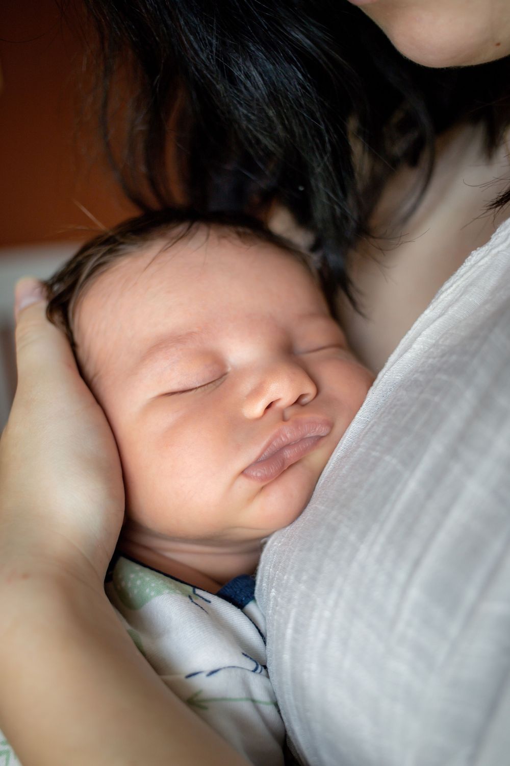 Close-up of a sleeping newborn baby cradled gently in their mothers arms.