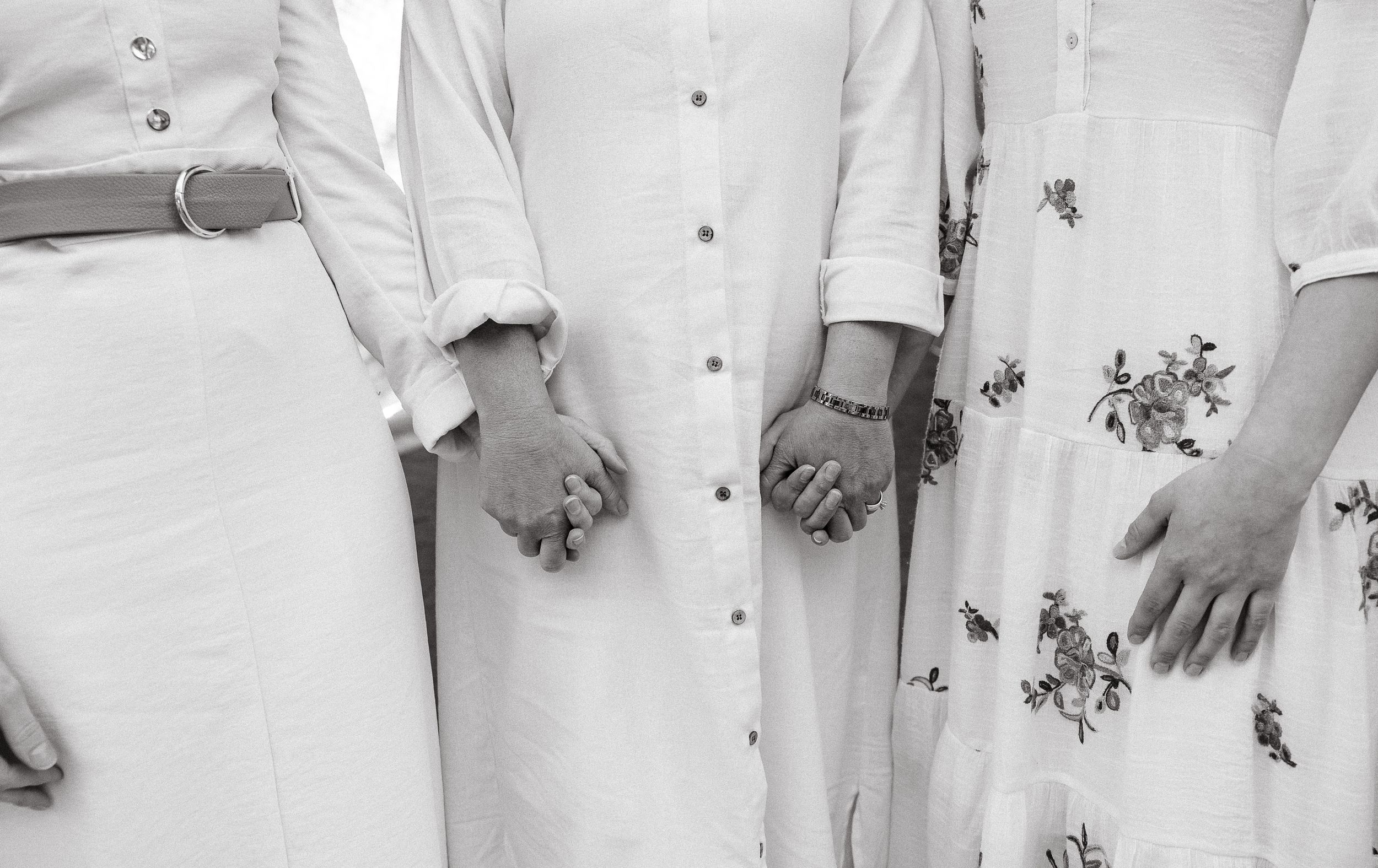 Wedding party members in white and neutral attire stand together for formal photo.