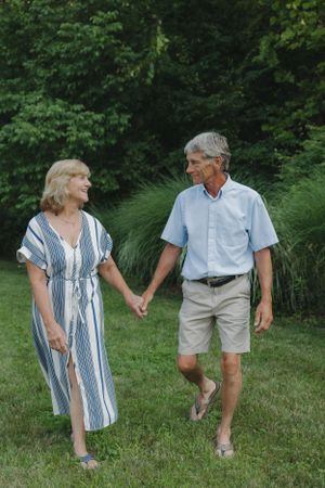 Couple in casual summer attire walking and laughing together in a green garden.