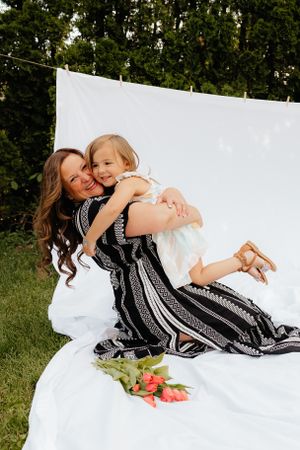 Mother and child lying on white blanket outdoors sharing playful cuddles.