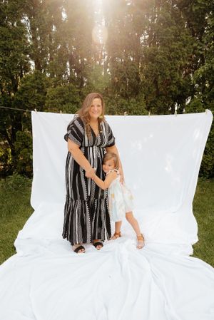Woman in striped dress sitting on white backdrop in outdoor sunlit setting.