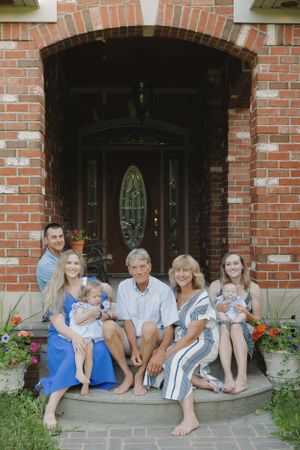 Extended family poses casually on brick porch steps during outdoor photo session.