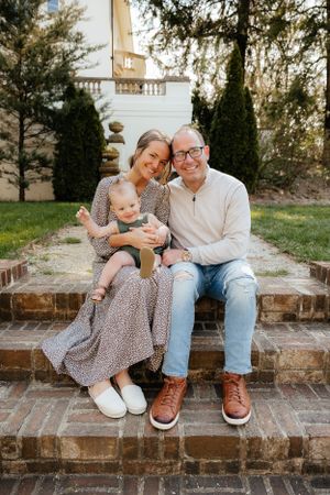 Family sitting together on brick steps outdoors surrounded by trees and greenery.