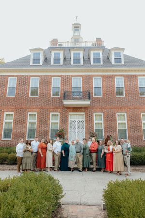 Large group portrait in front of historic brick building with white trim.