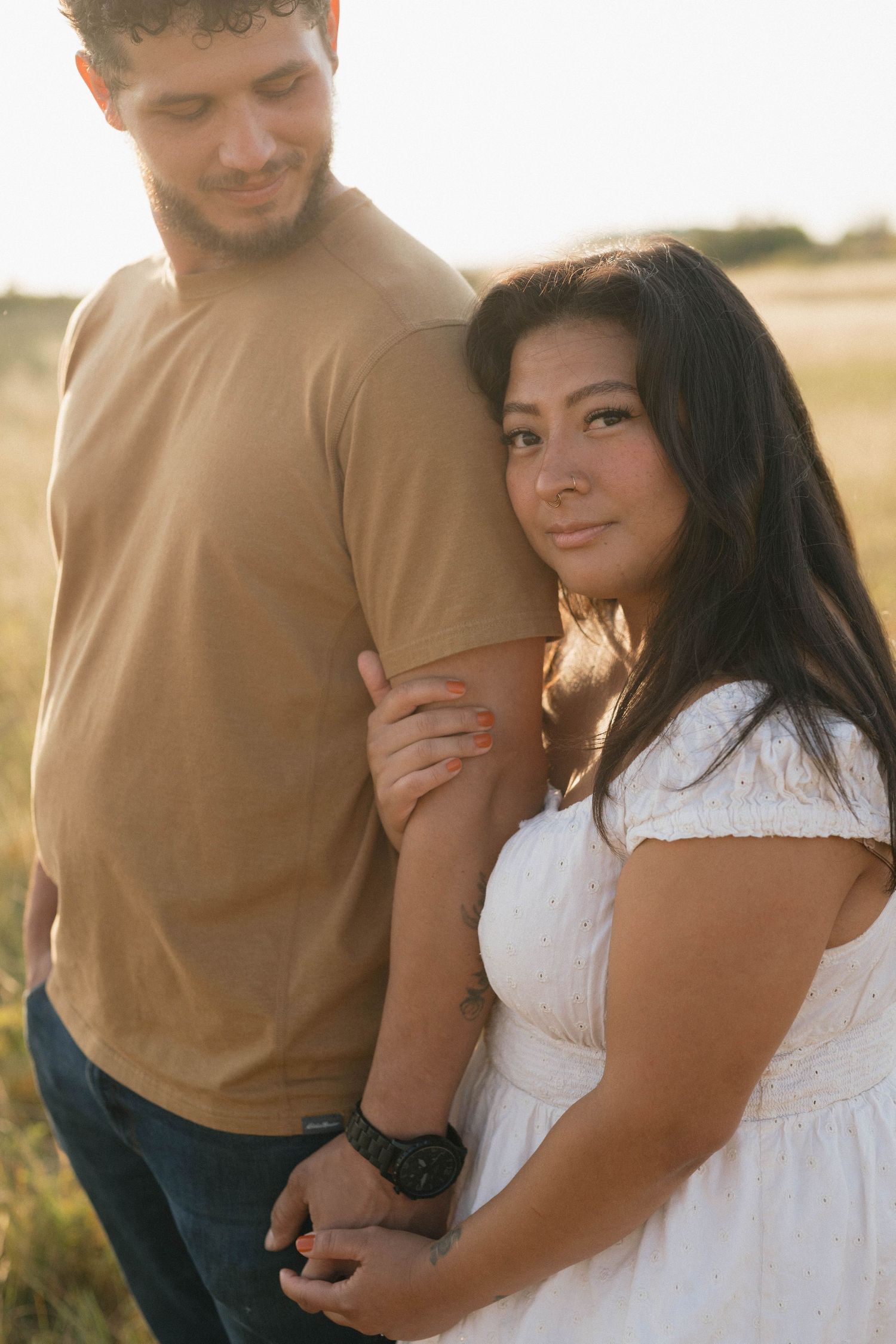 Romantic portrait of couple in warm sunlight, standing close together in a grassy field.