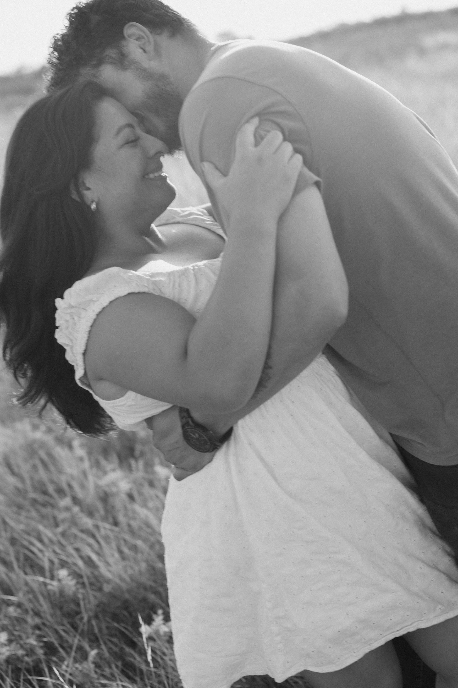 Black and white portrait of couple sharing an intimate embrace in tall grass.