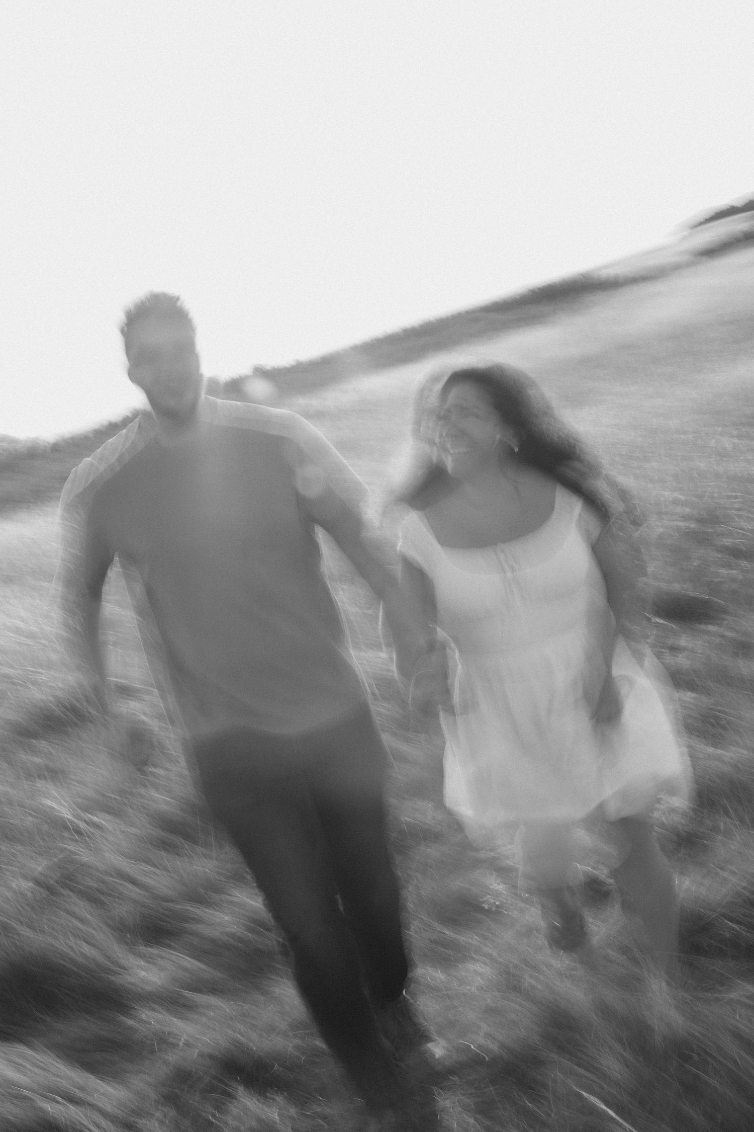 Motion-blurred black and white photo of couple running through a wind-swept field.
