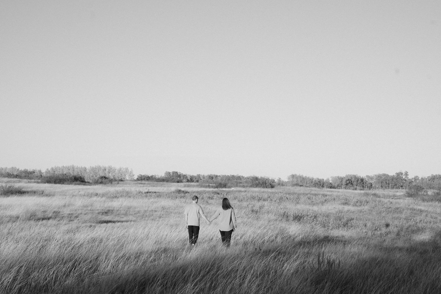Black and white photograph of two people walking together through a vast grassy meadow.