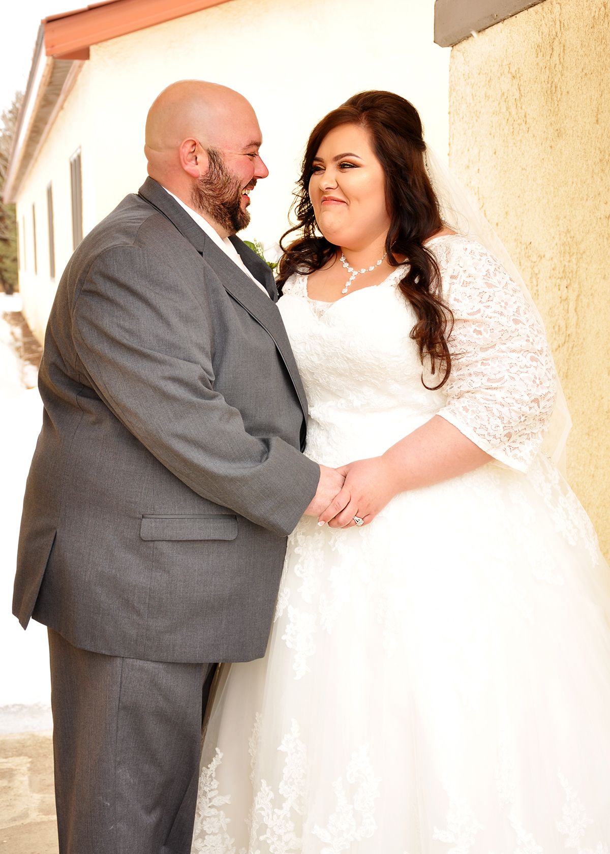 Romantic wedding couple in grey suit and white dress sharing intimate moments.