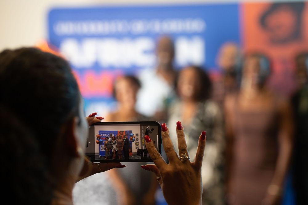 Someone takes a photo on their phone at an event with blurred figures in the background.