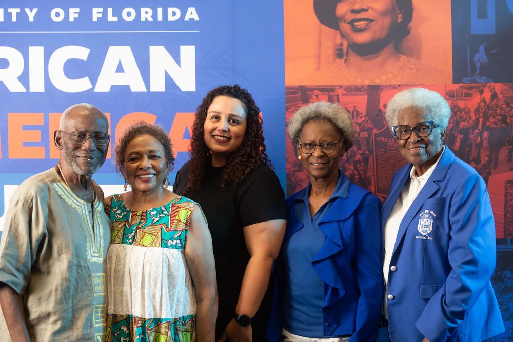 Group of five people posing together at University of Florida event with historic photo display backdrop.