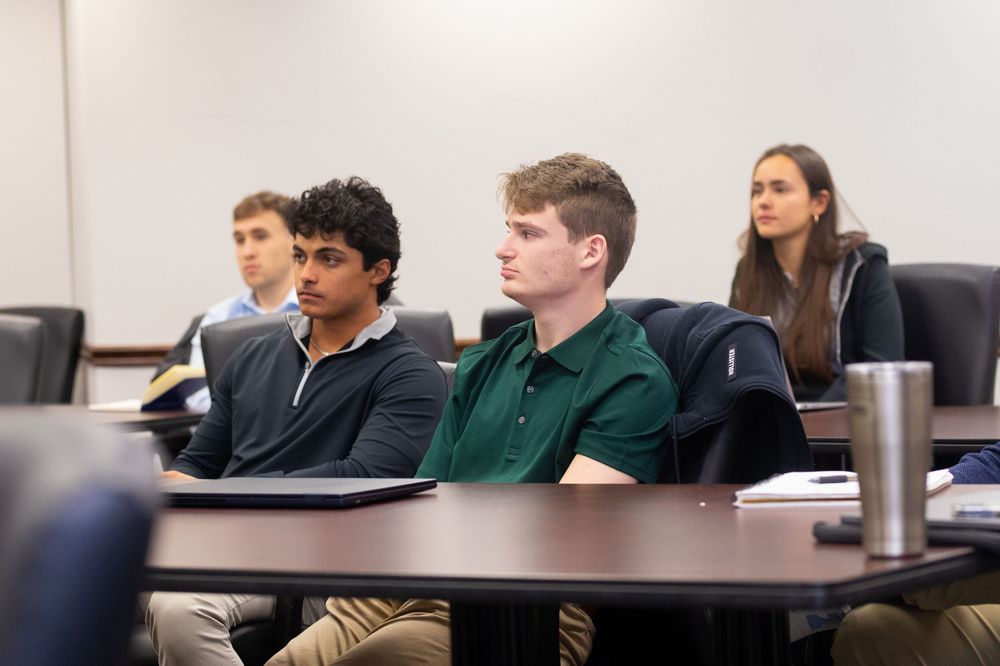 Students sit attentively at desks during a lecture in a modern classroom.