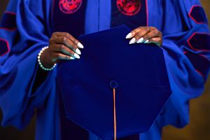 Close-up of hands in graduation regalia holding blue graduation cap.