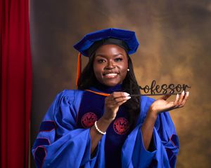 Graduate in blue academic regalia poses with nameplate during graduation photoshoot.